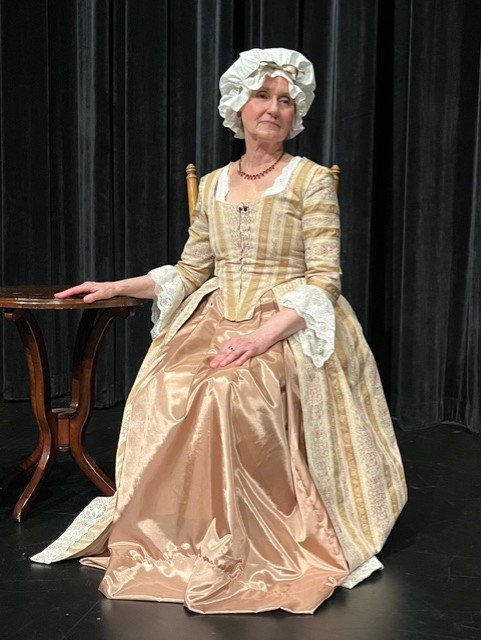 Woman dressed in 18th century period costume sitting beside of a table